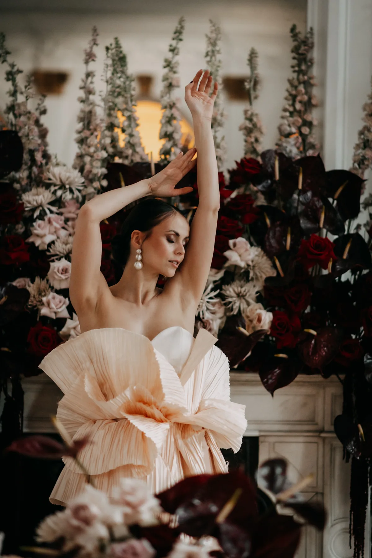 Fine-Art-Editorial – Model in Pfirsich-Couture-Robe am Kamin mit Bordeaux-Floristik